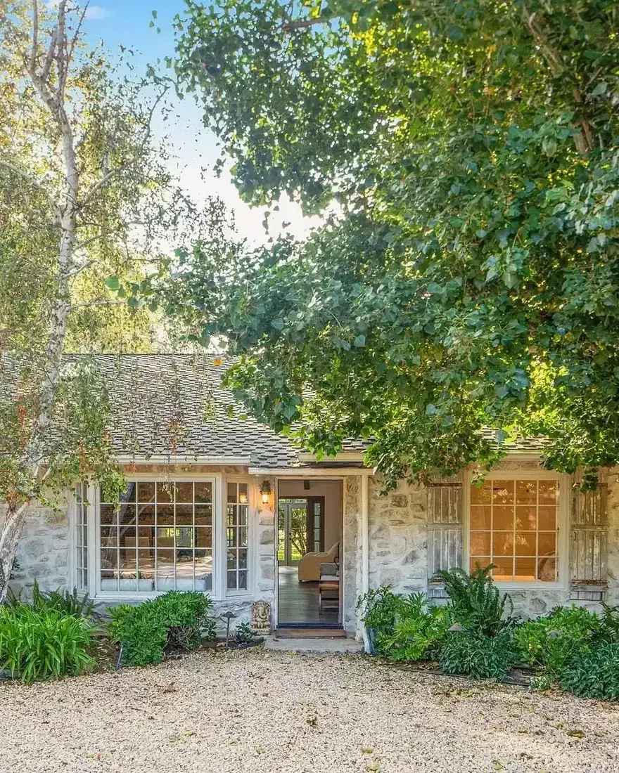 Pale limewashed stone cottage with an open door, steel windows, and a gravel forecourt to the walls