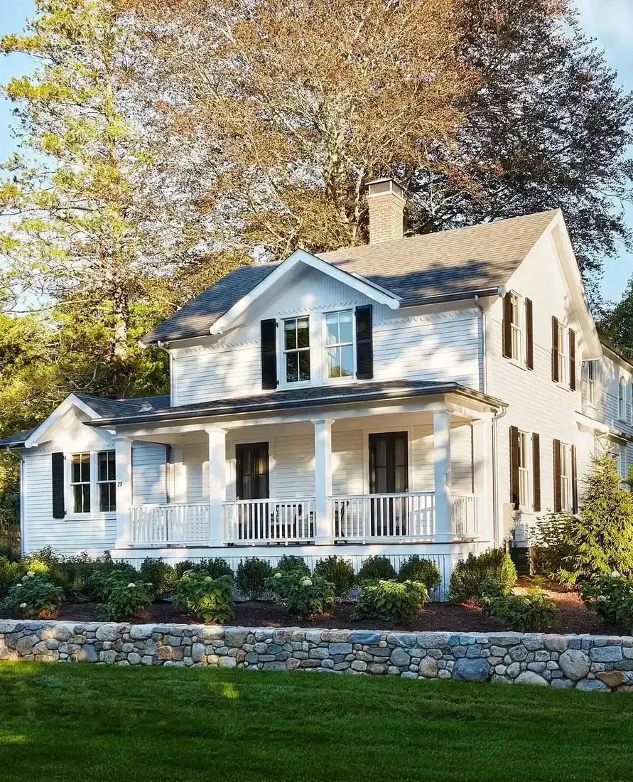 White farmhouse with wraparound porch and low stone wall along the front