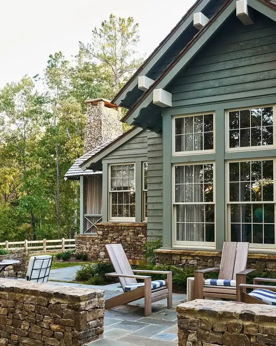 Sage green cottage with stone chimney and stone patio walls with timber loungers