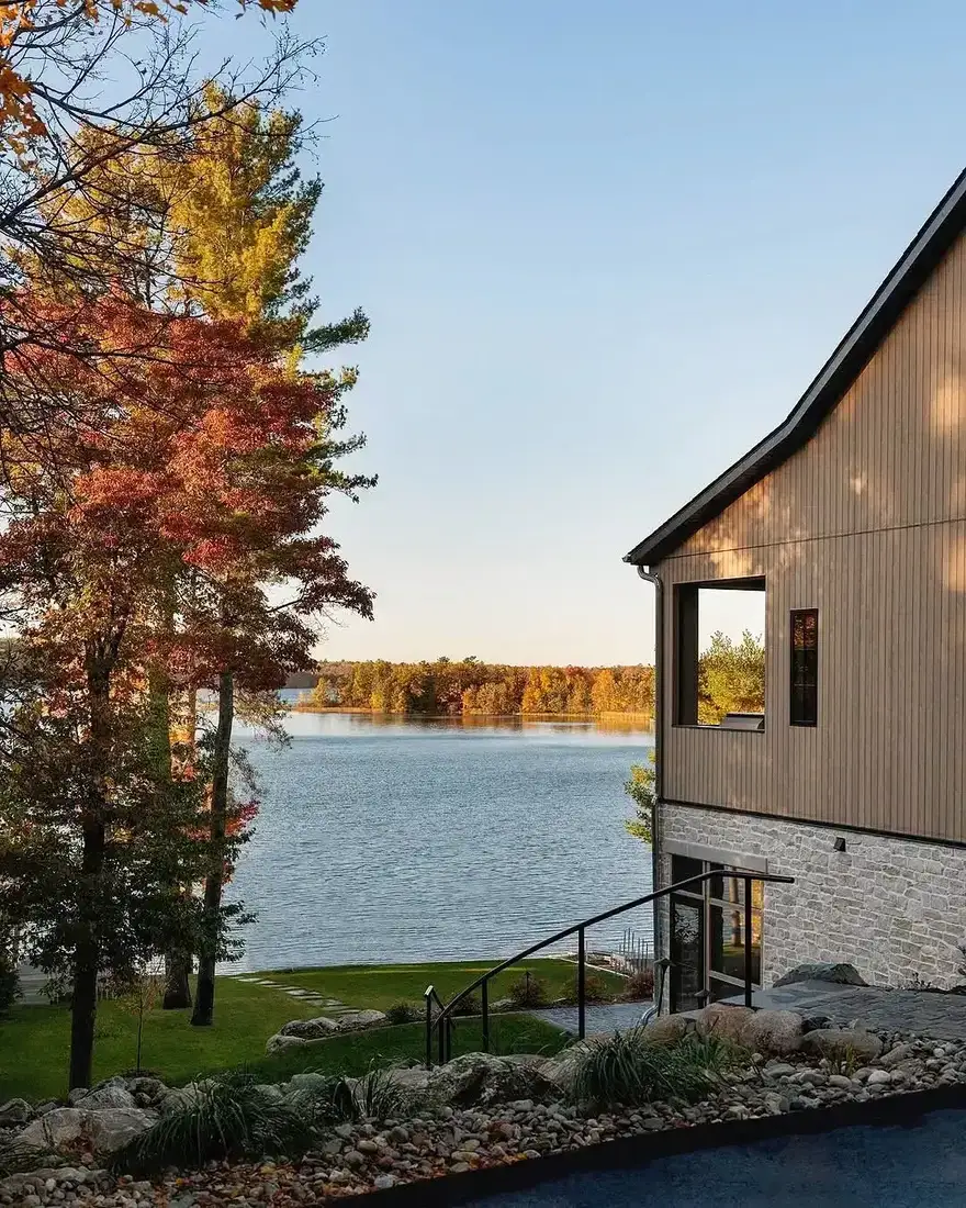 Modern house with vertical timber siding over a pale stone base beside a lake