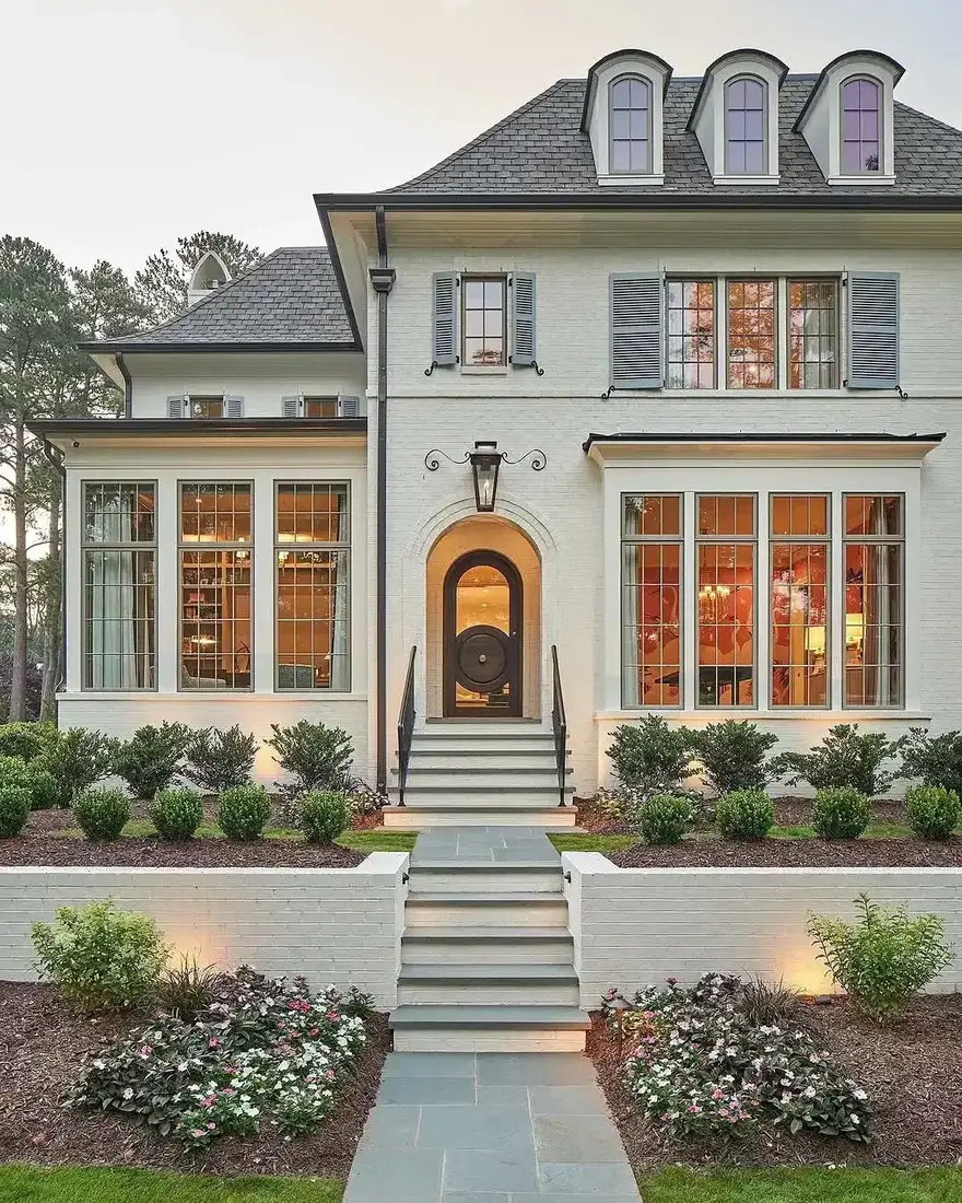 White painted house front with a dark arched door, grey shutters, and wide slate steps