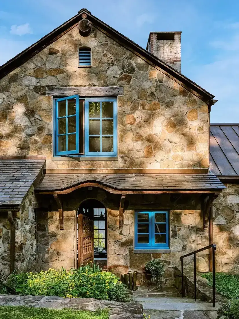 Rubble stone gable with bright blue windows and an arched oak door under a curved slate hood