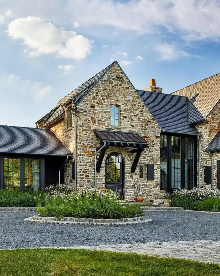 Buff rubble stone gable with black steel windows and a gravel forecourt edged in setts