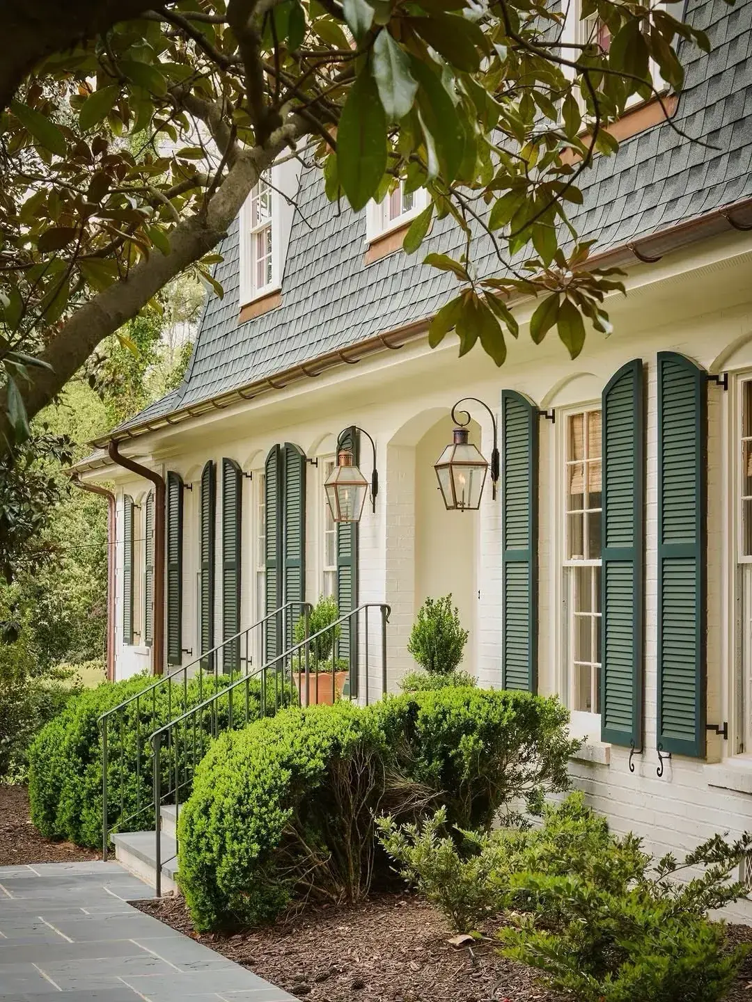 Cream rendered house with arched window heads, green louvered shutters and gas lanterns