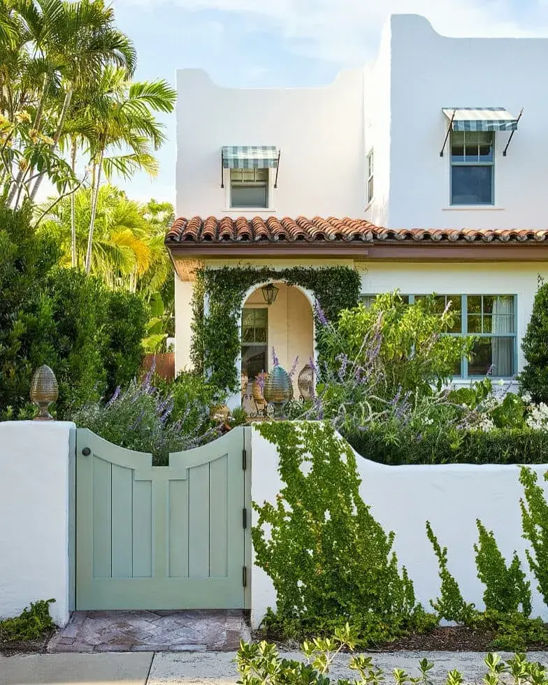 White stucco wall with a sage green timber gate, capped piers and a tiled Mediterranean house behind