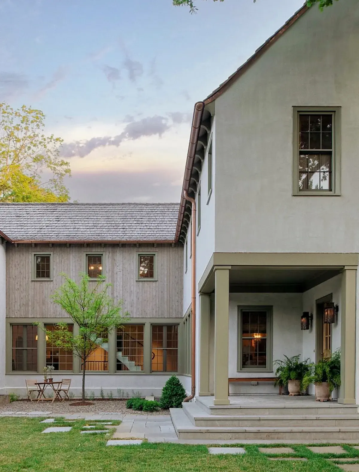 Pale sage rendered farmhouse with a covered porch, square piers and copper downpipes