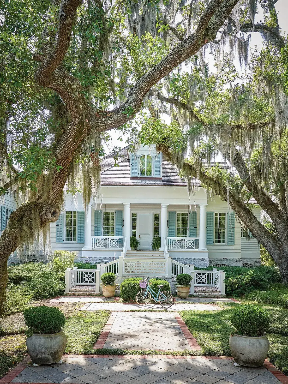 White Southern cottage with pale blue shutters, a columned porch and Spanish moss in the oaks