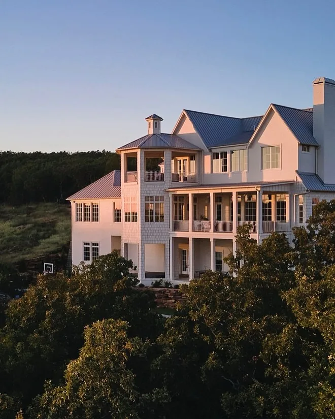 Large pale coastal house with double porches, tower and grey metal roof at dusk