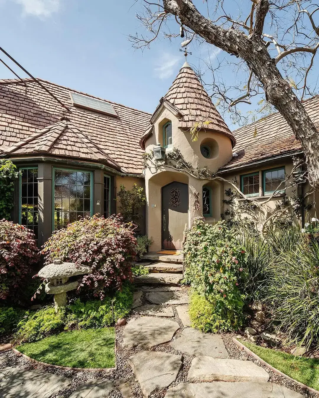 Stucco cottage with conical shingle turret, green window frames and stone path