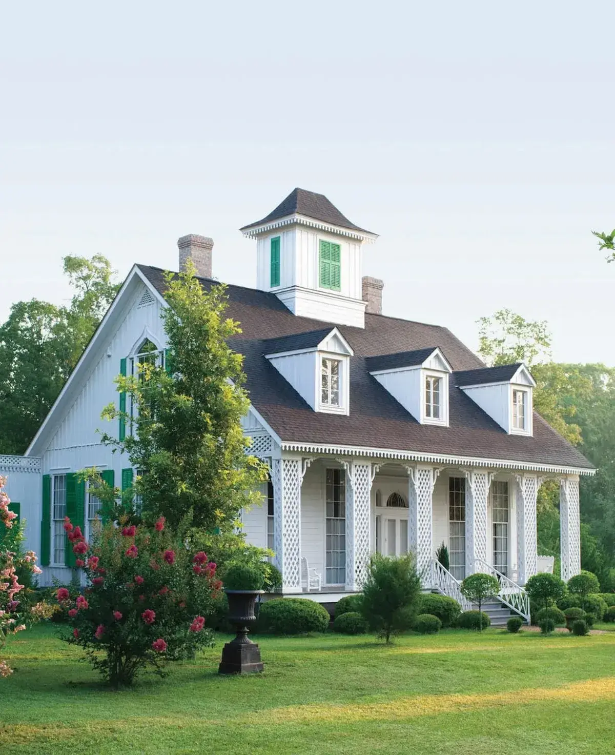 White clapboard house with dark green shutters, lattice porch posts and roof cupola