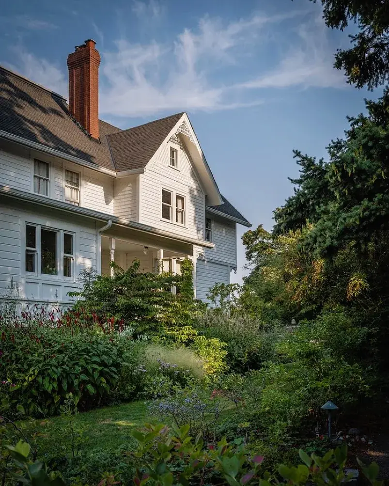 White gabled house with brick chimney, gable fret and cottage planting