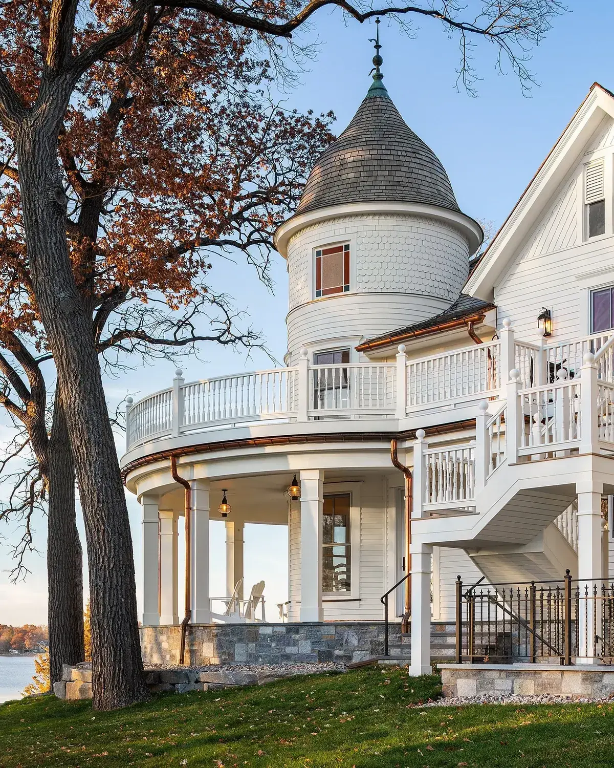 White lakeside turret house with curved porch, copper pipes and stone base