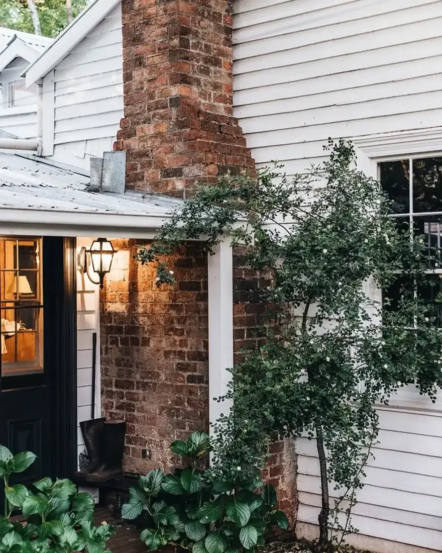 Red brick chimney against white clapboard with a black lantern, black door and boots on a porch