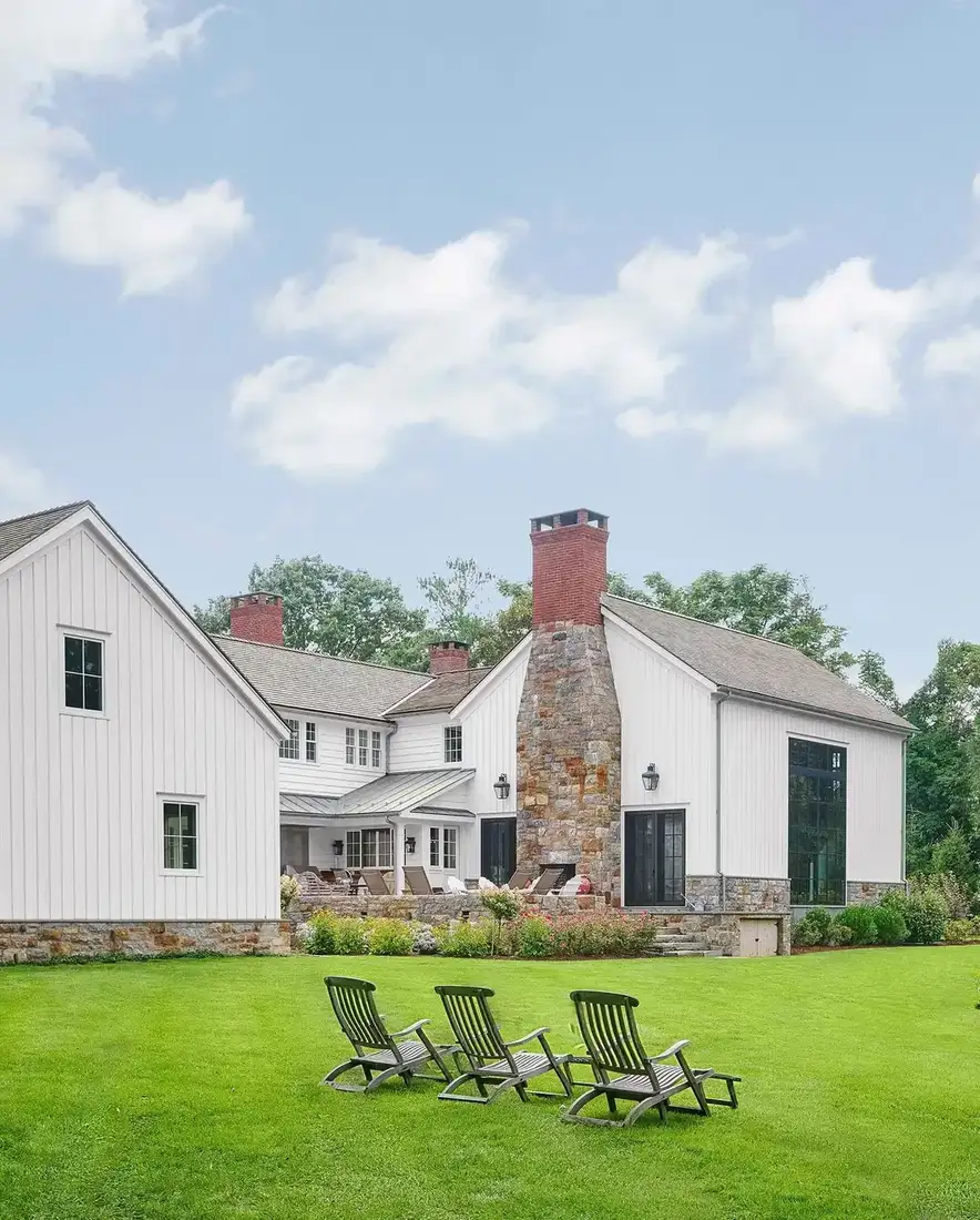White board and batten farmhouse with stone chimney and dark framed glass