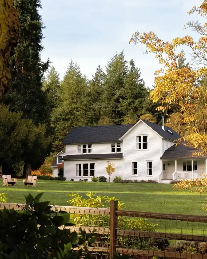 White farmhouse with black roof behind a timber post and rail fence in a meadow