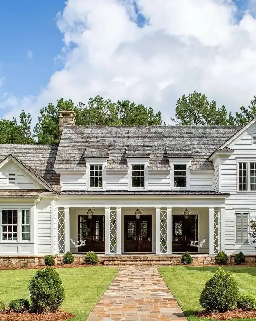 White symmetrical farmhouse with dark French doors, grey shingle roof and flagstone path