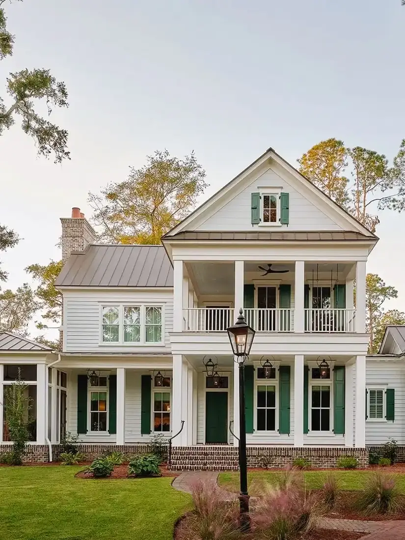 White double height farmhouse with deep green shutters and grey metal roof