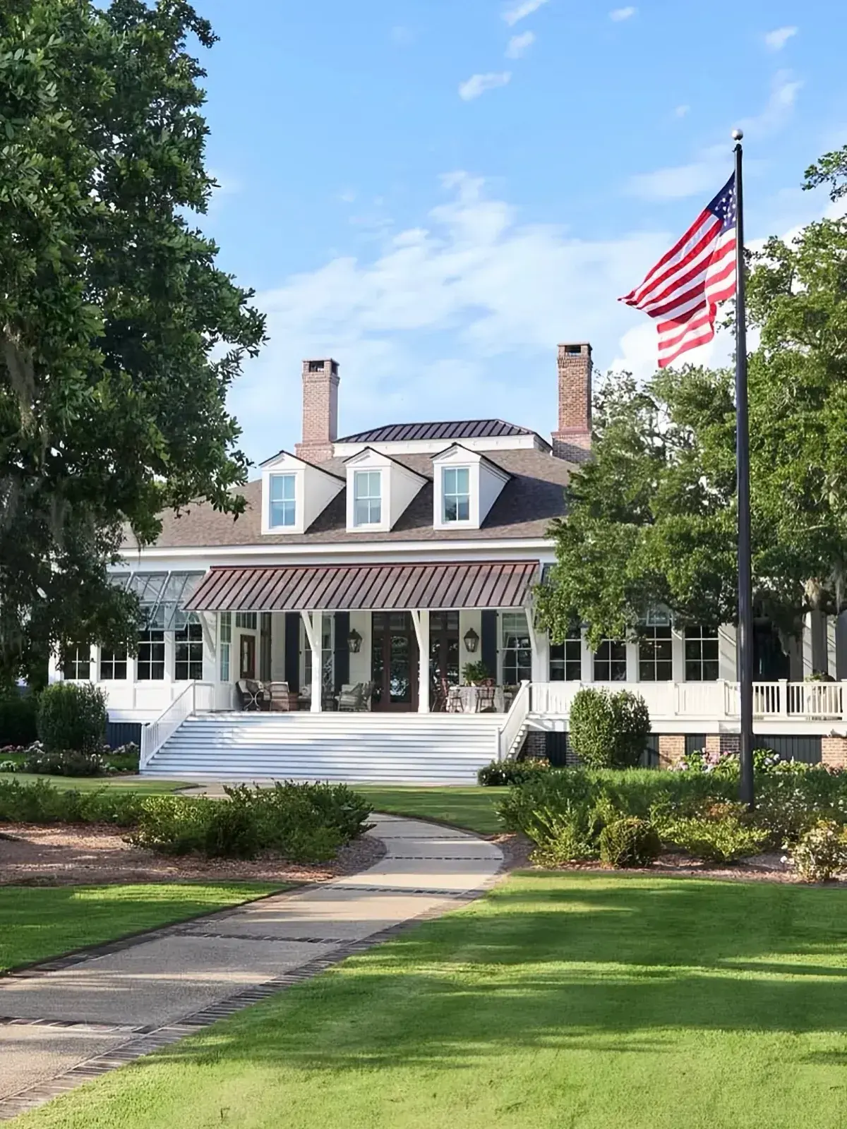 White low country house with copper porch roof, dormers and brick chimneys