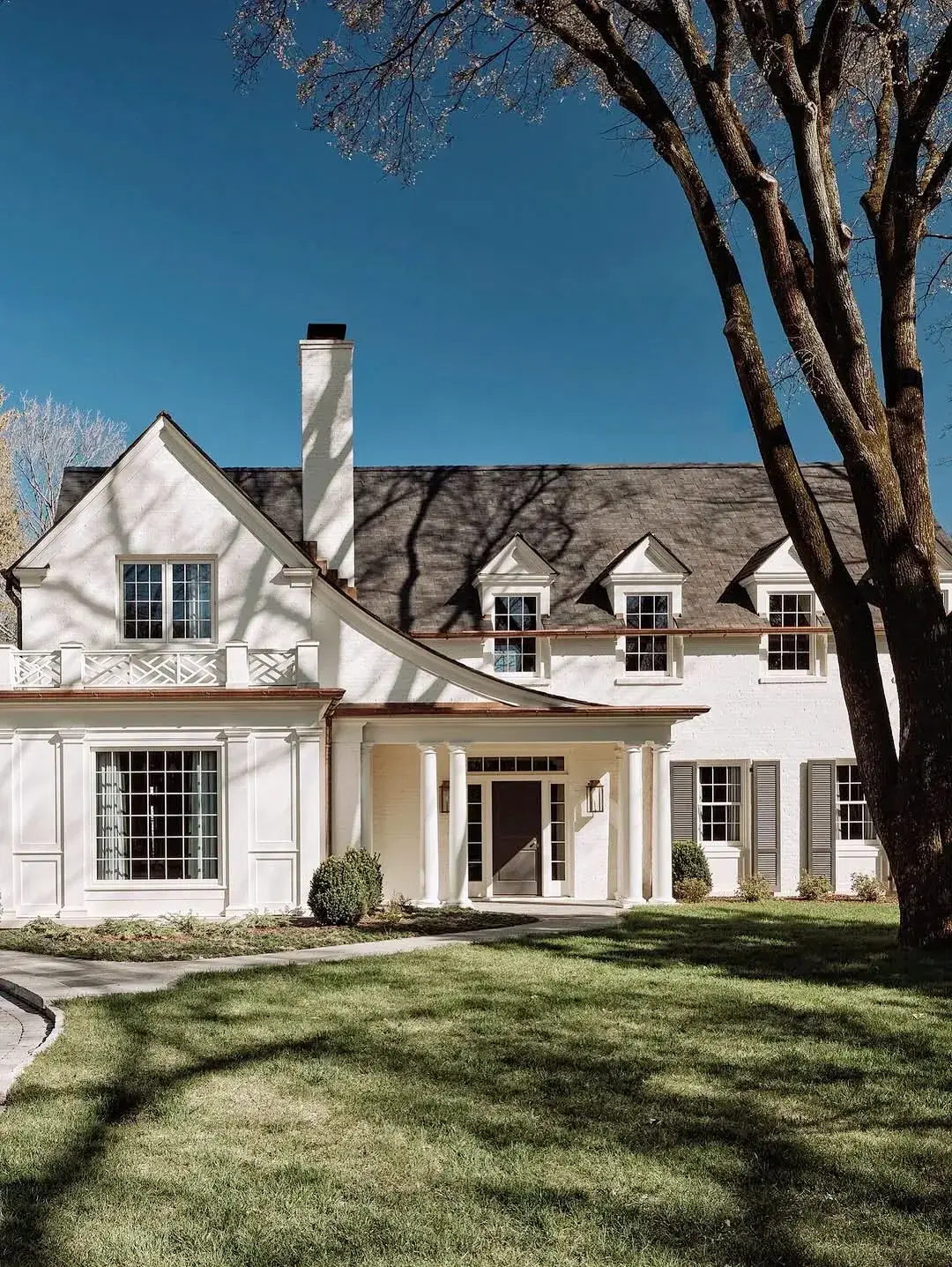 White brick house with copper gutters and dormers under bare trees