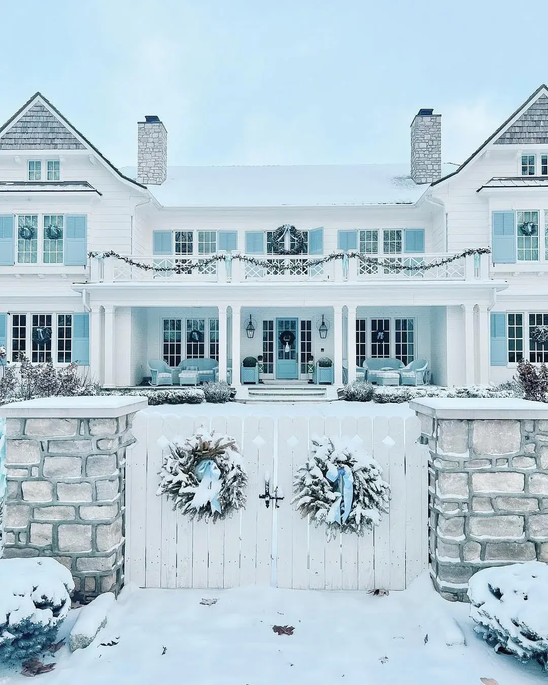White house with blue shutters and gate wreaths in deep snow