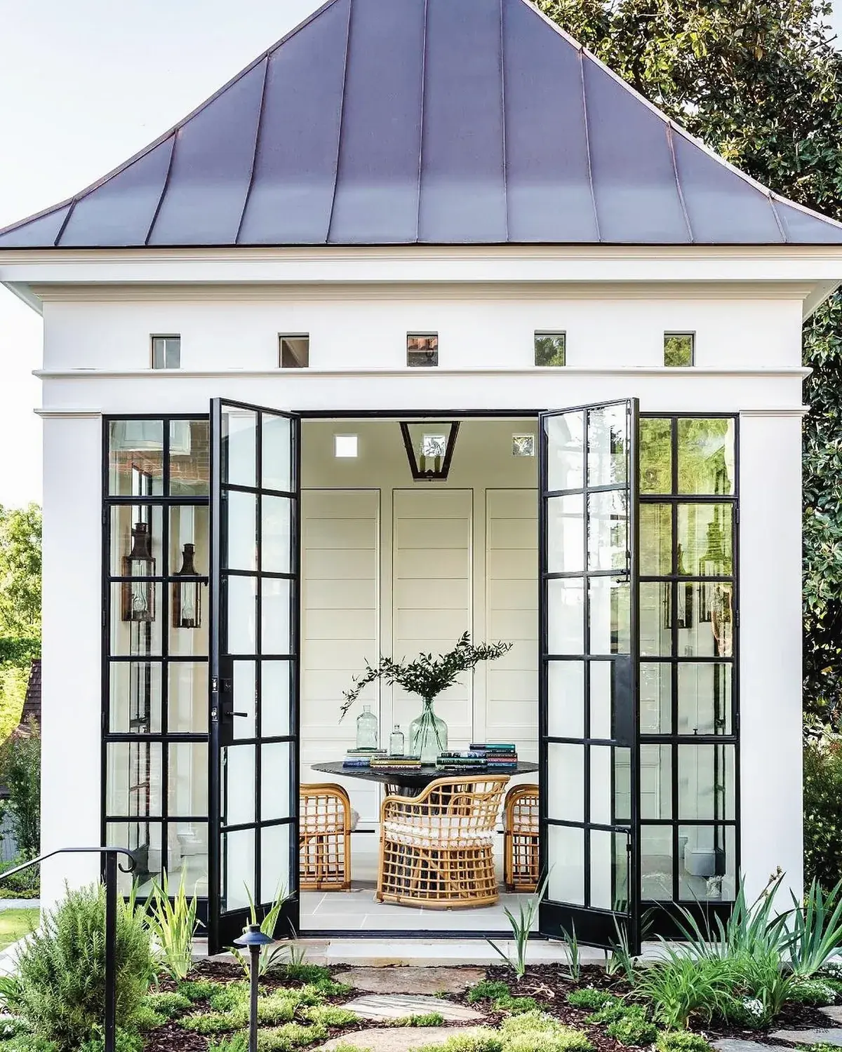White pool house with black steel doors open to rattan chairs