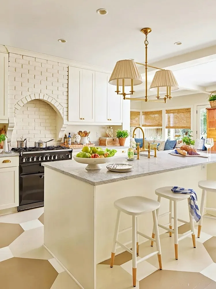 White painted brick arch over a range with a brass chandelier above the island
