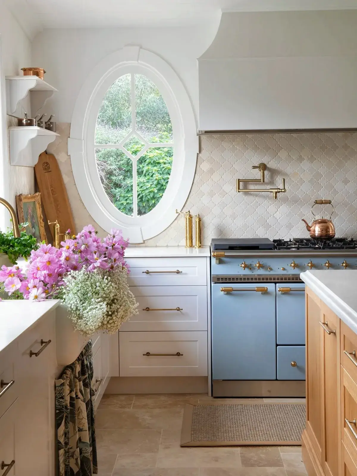 White kitchen with a pale blue range cooker, an oval window and brass fittings