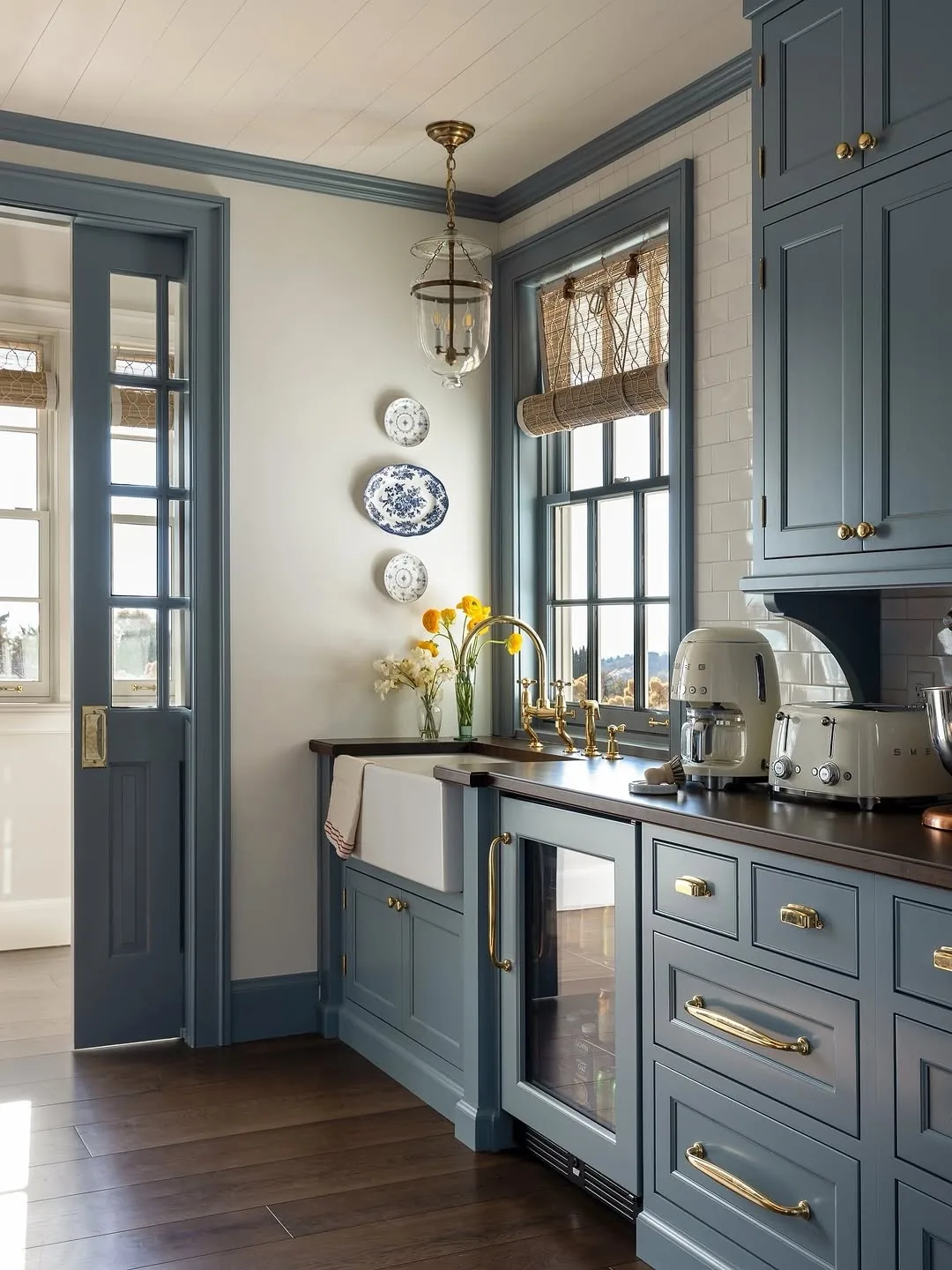 Slate blue kitchen with a glazed door painted blue, brass tap and dark worktop