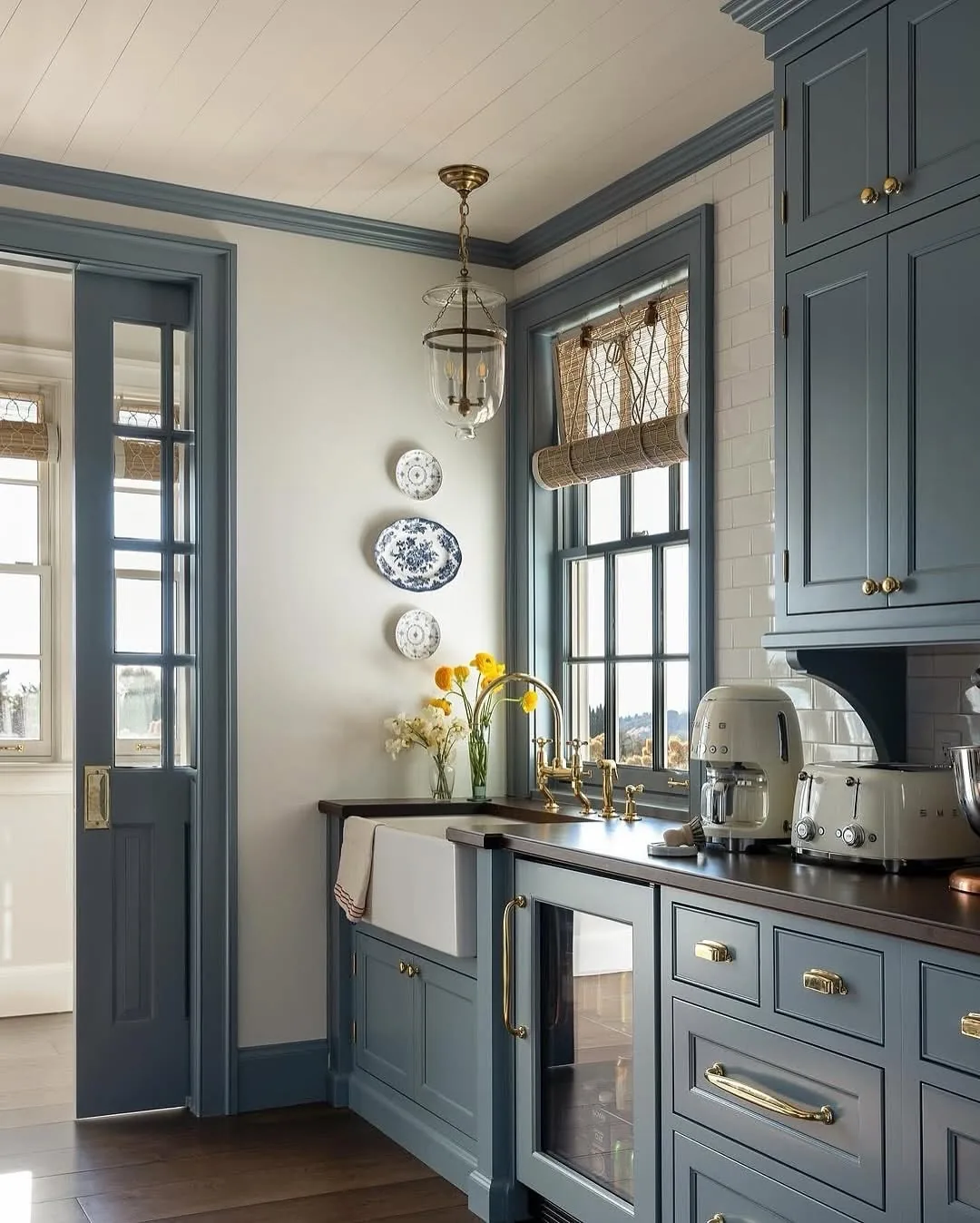 Slate blue sink run with brass hardware, a woven blind and a glass lantern
