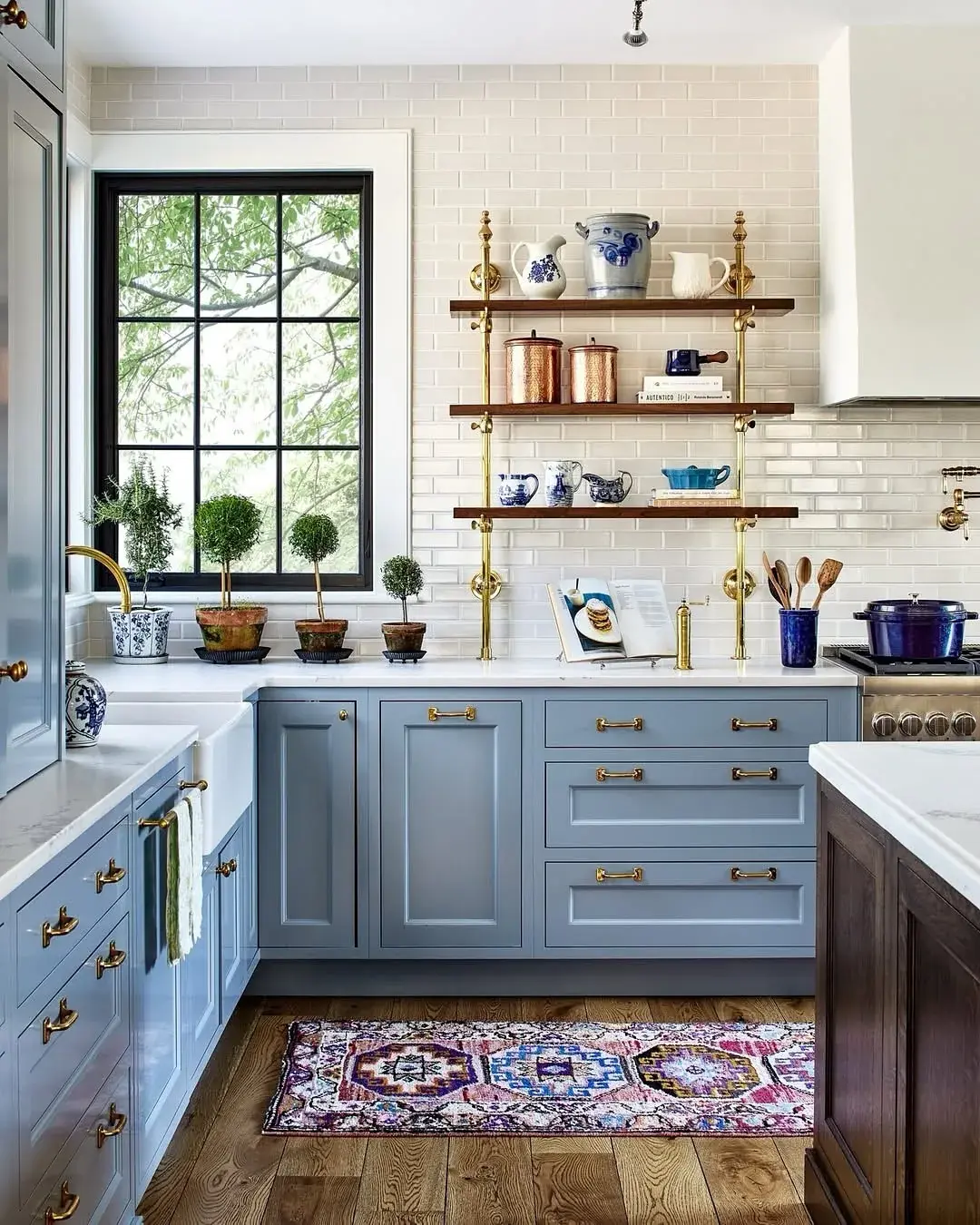 Dusty blue kitchen with brass gantry shelves, copper pots and a black framed window