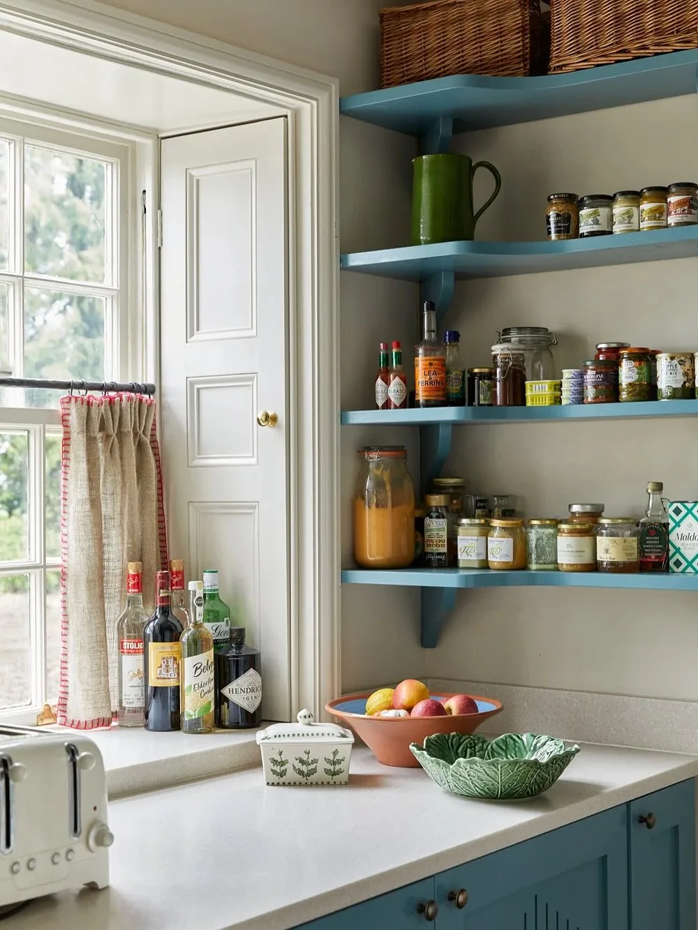 Pantry corner with blue open shelves holding jars beside a linen curtain