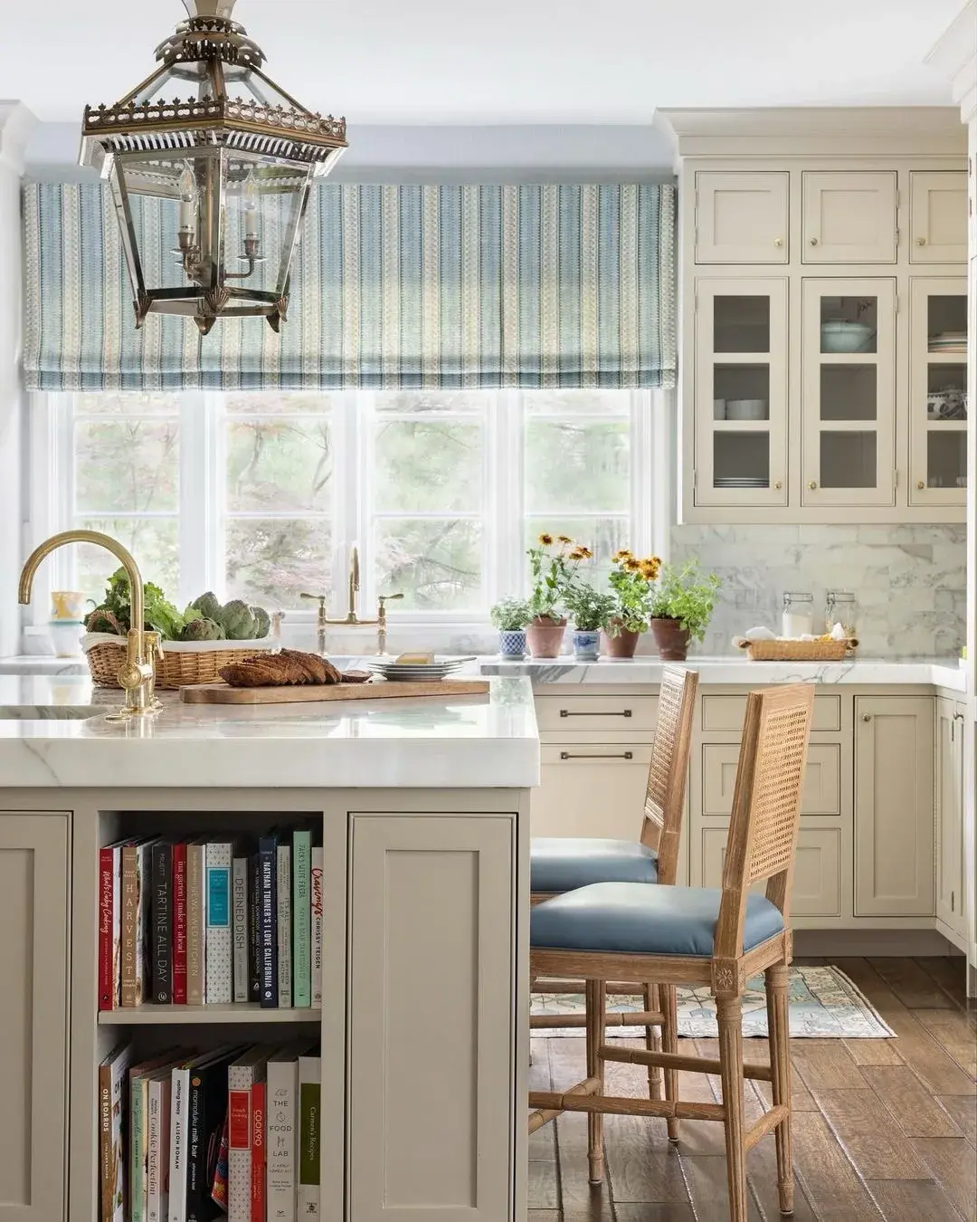 Cream kitchen with a blue striped blind, cane chairs and a marble island