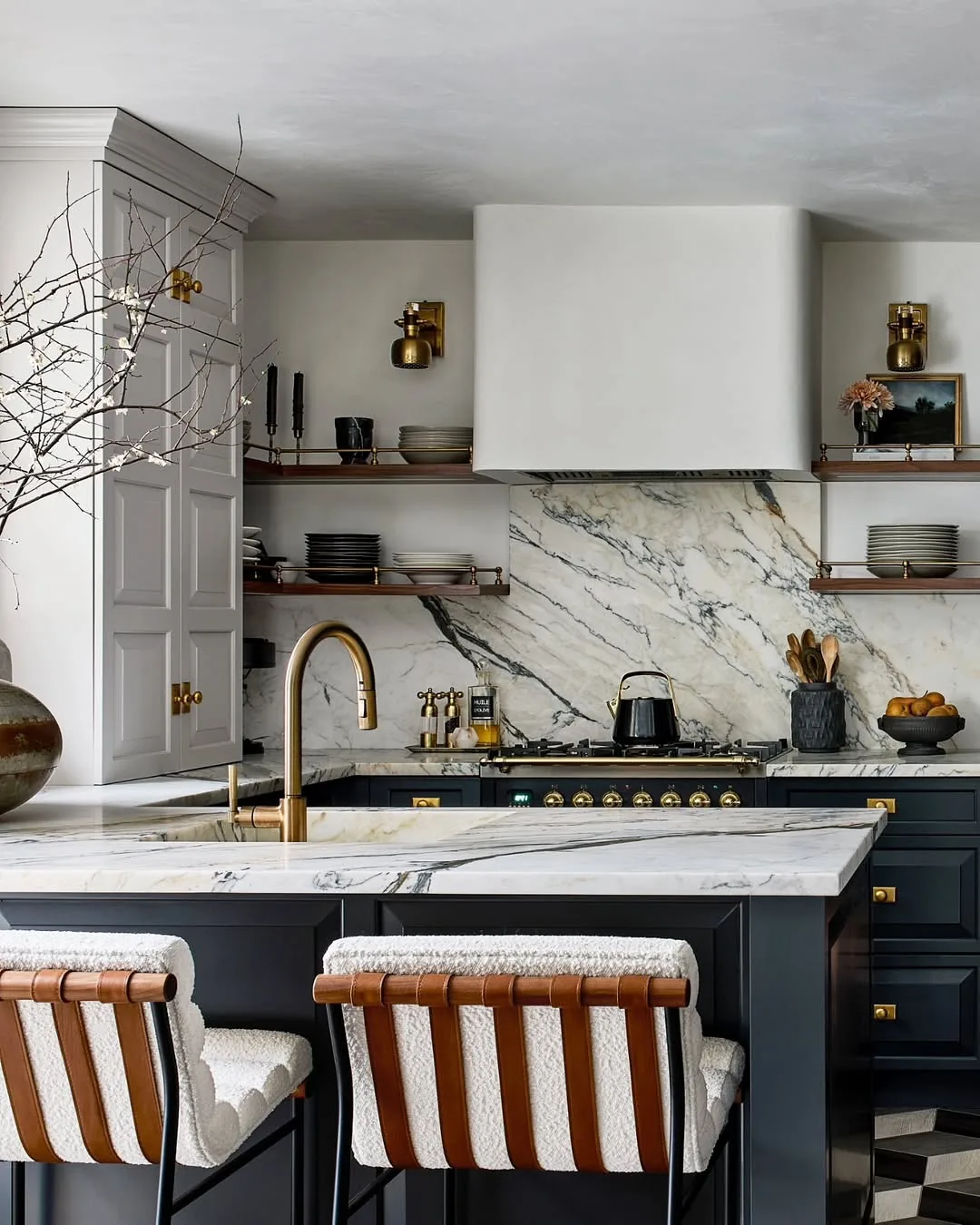 Navy island with veined marble splashback, brass lights and boucle stools