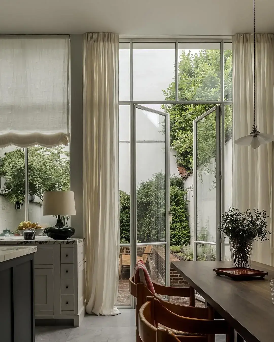 Tall steel framed garden doors with full height linen curtains and a timber dining table
