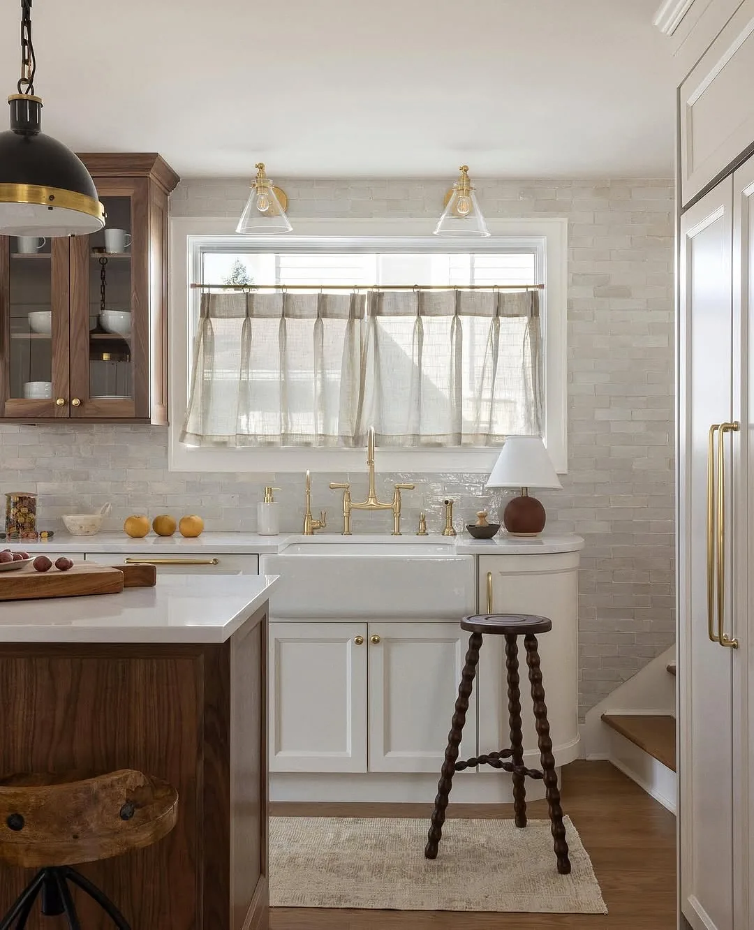 Wide sink window with sheer cafe curtain on a brass rod, brass bridge tap and walnut cabinetry