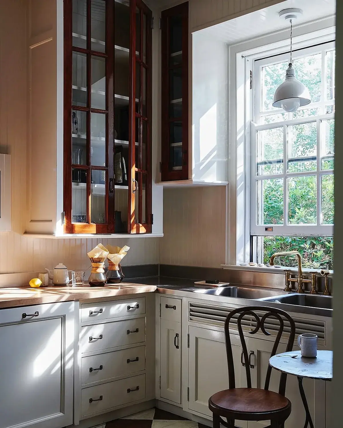 Small corner sink window with mahogany glazed cupboards, timber top and bentwood chair at a marble table