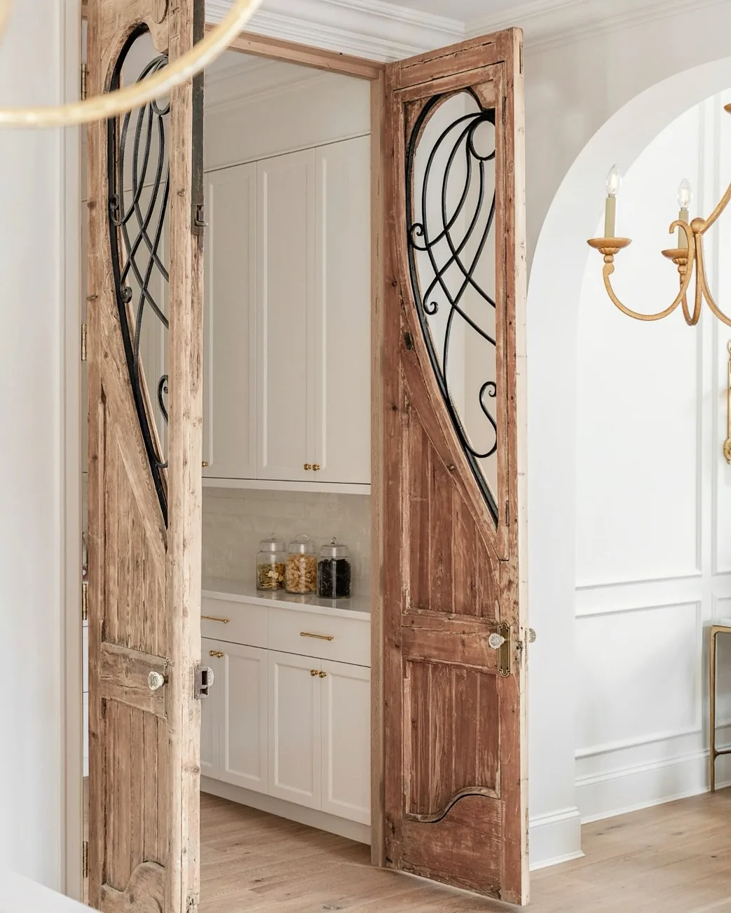 Salvaged timber doors with wrought iron grilles opening onto a plain white scullery
