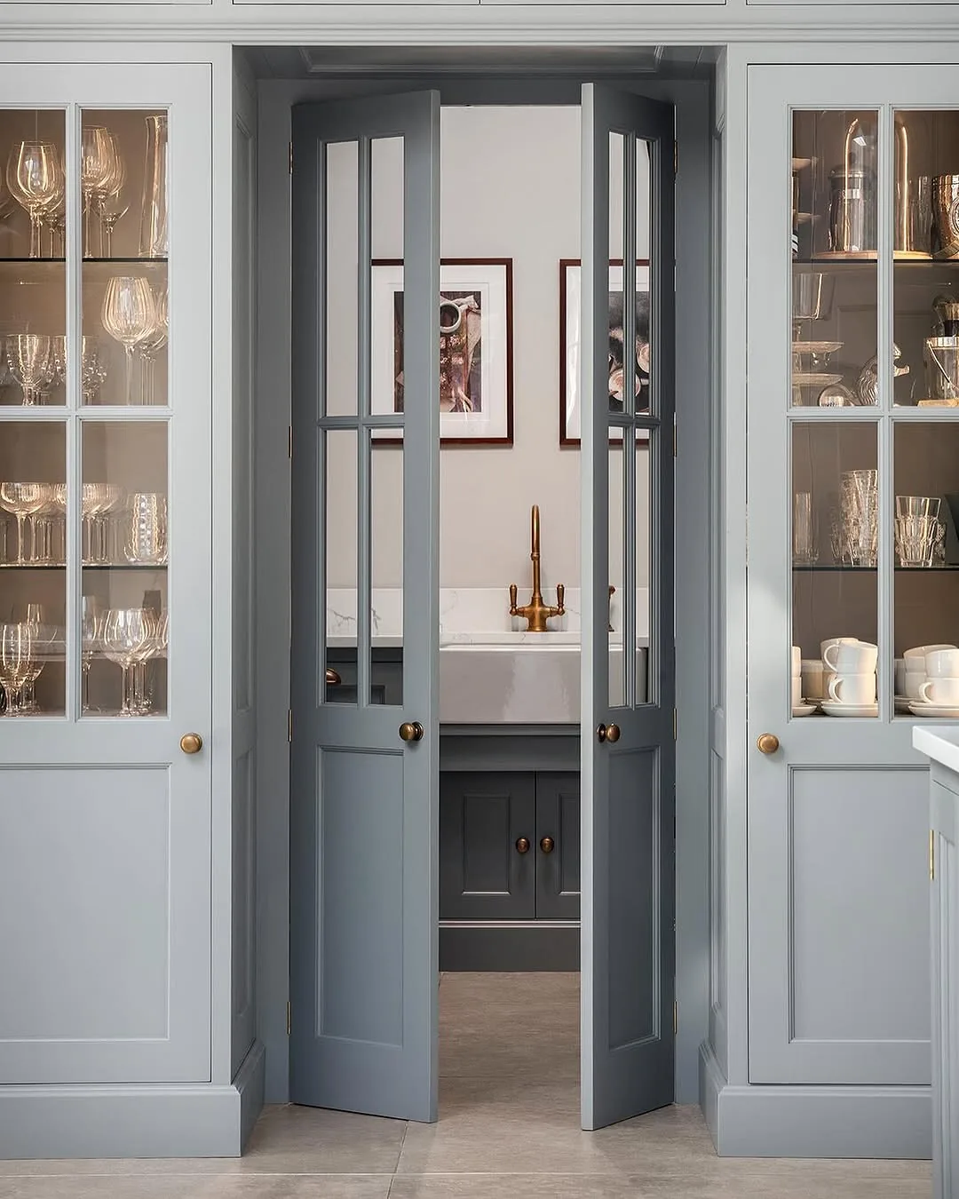 Pale grey double glazed pantry cupboards flanking double doors to a sink with a brass tap