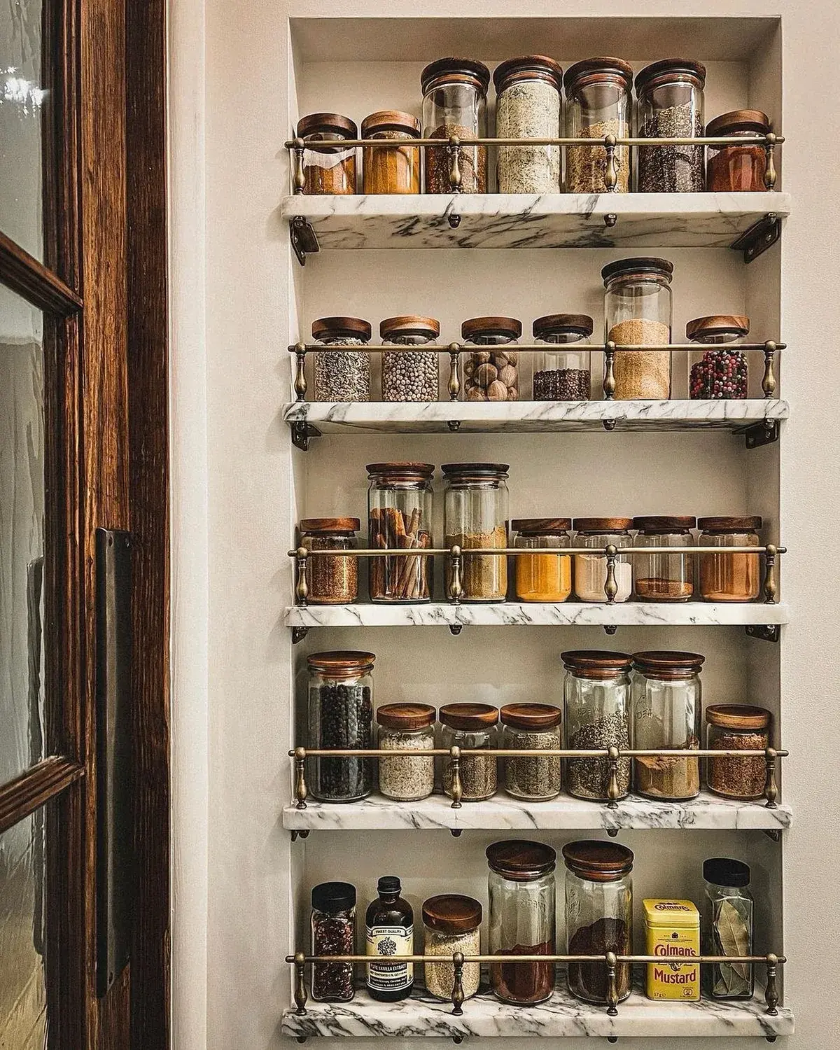 Recessed marble shelves with brass gallery rails holding uniform glass jars