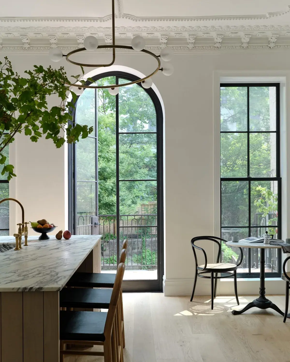 Pale kitchen with a marble island, brass tap and tall arched black steel windows