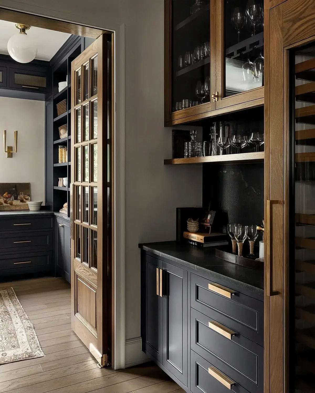Dark pantry cabinets with brass pulls, glazed wall cupboards and a timber wine fridge