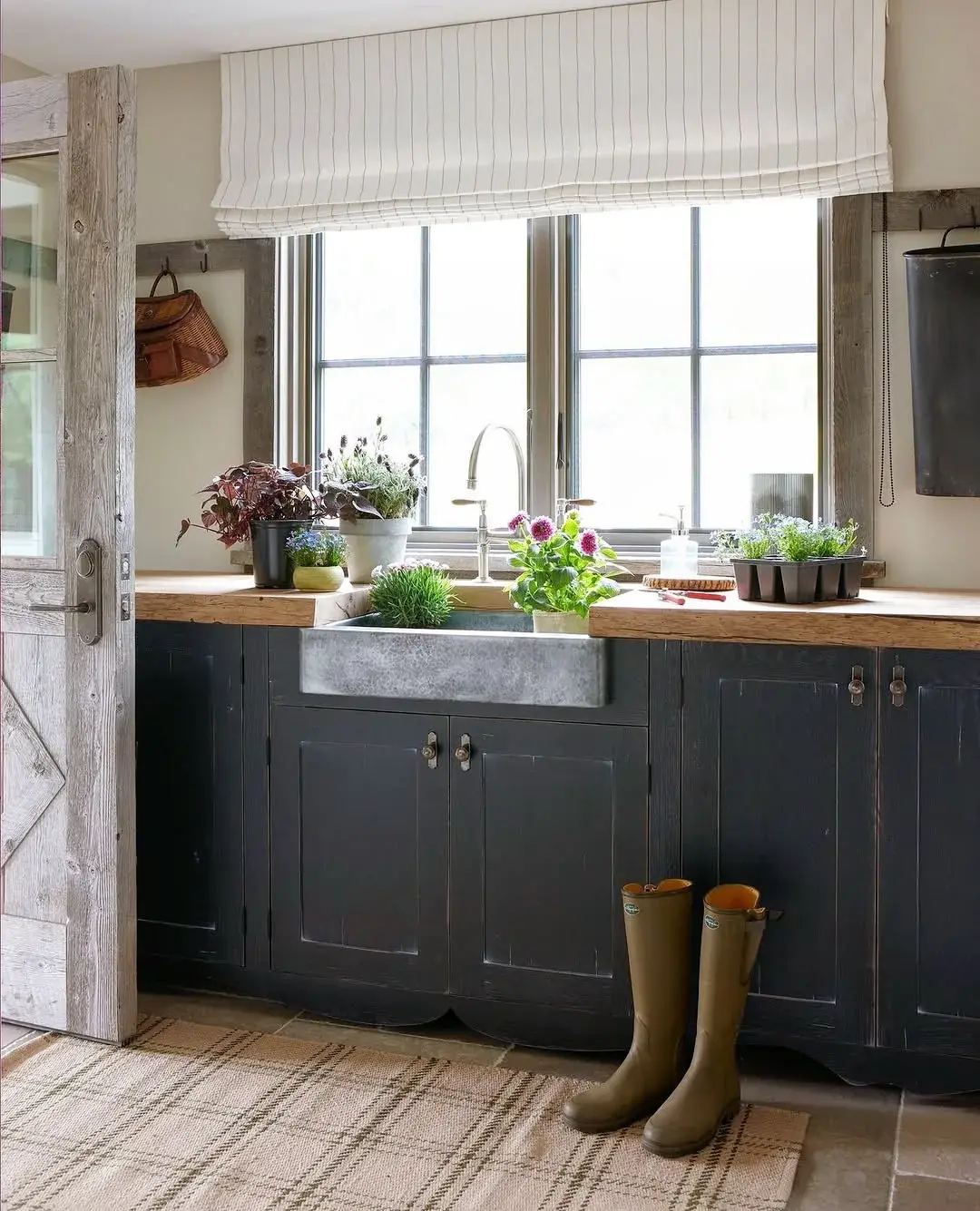 Black lower cabinets with thick timber tops and a metal farmhouse sink under a wide window