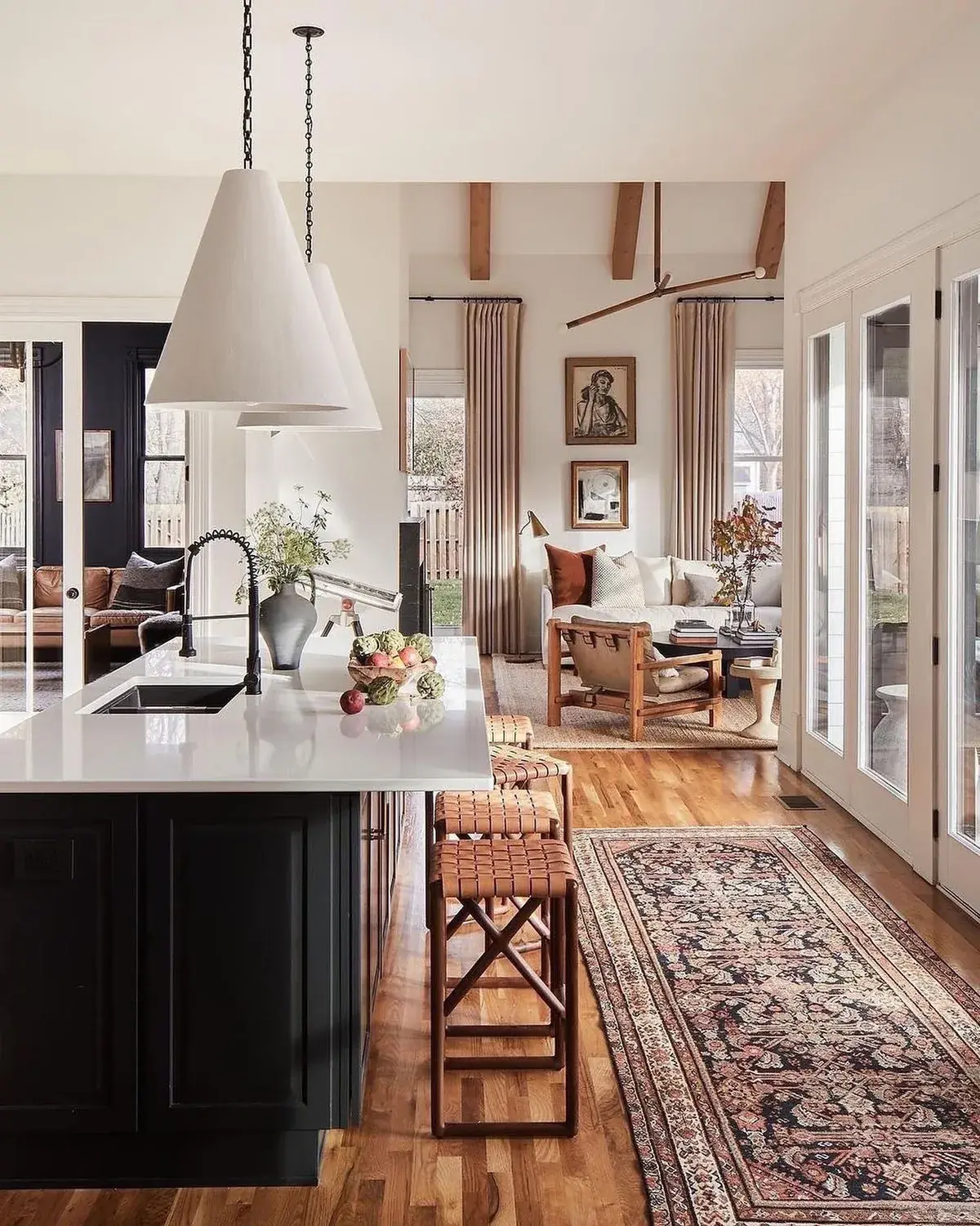Black island with a white top and twin cone pendants in an open plan kitchen
