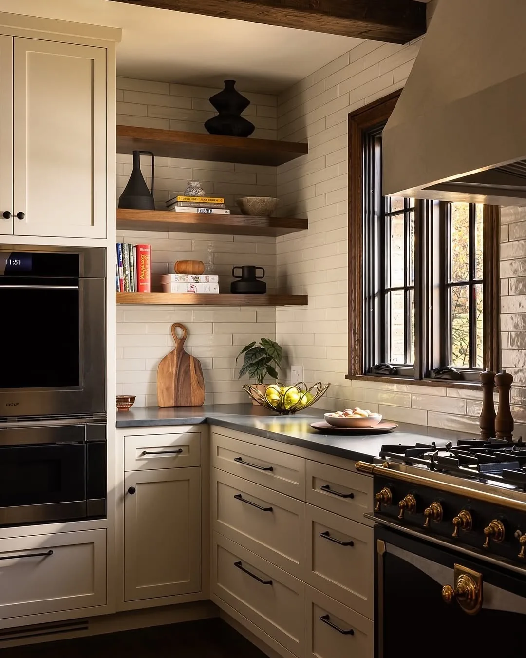 Cream kitchen with a black range, brass rails and walnut floating shelves