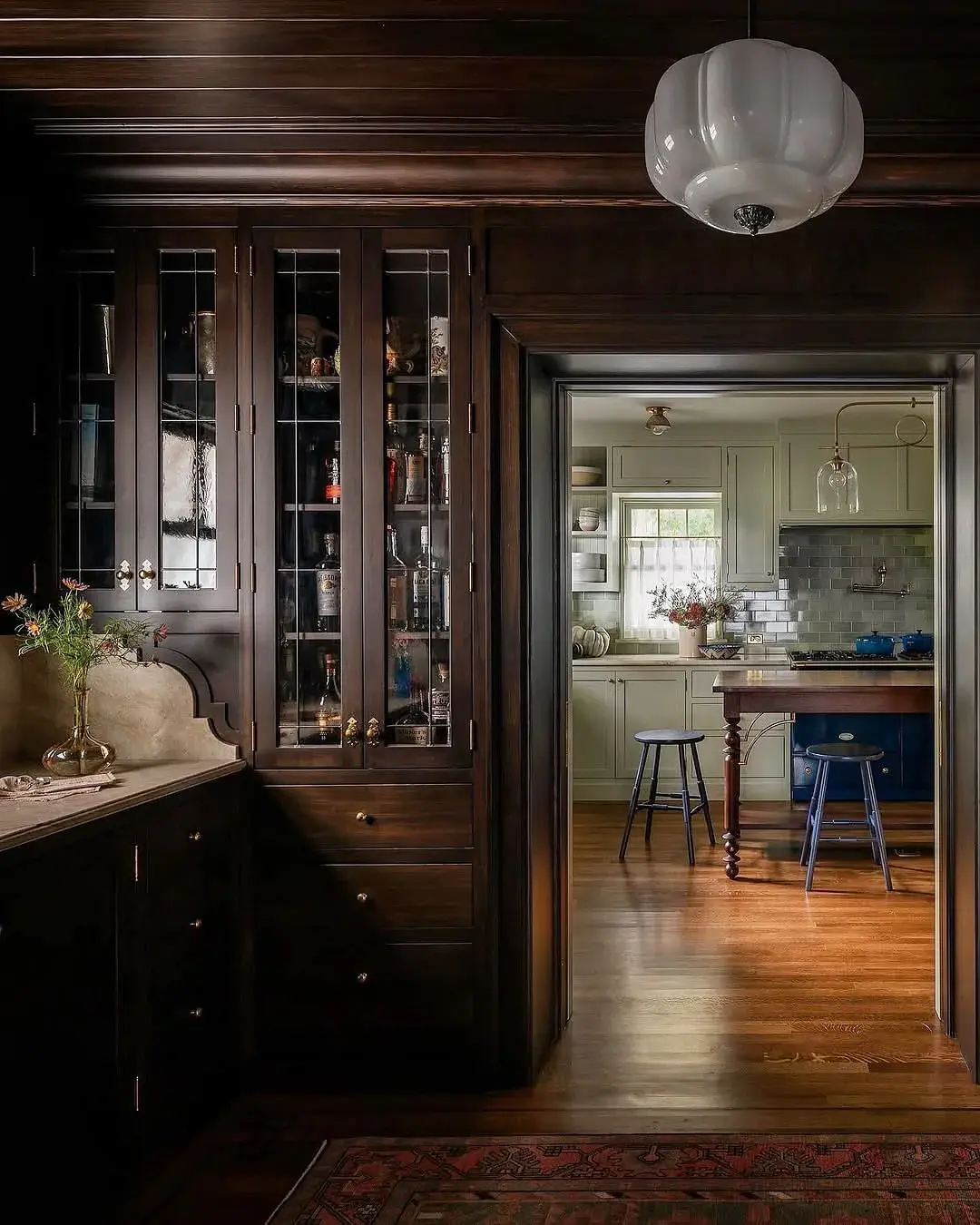 Dark timber pantry with glazed doors opening onto a pale green kitchen