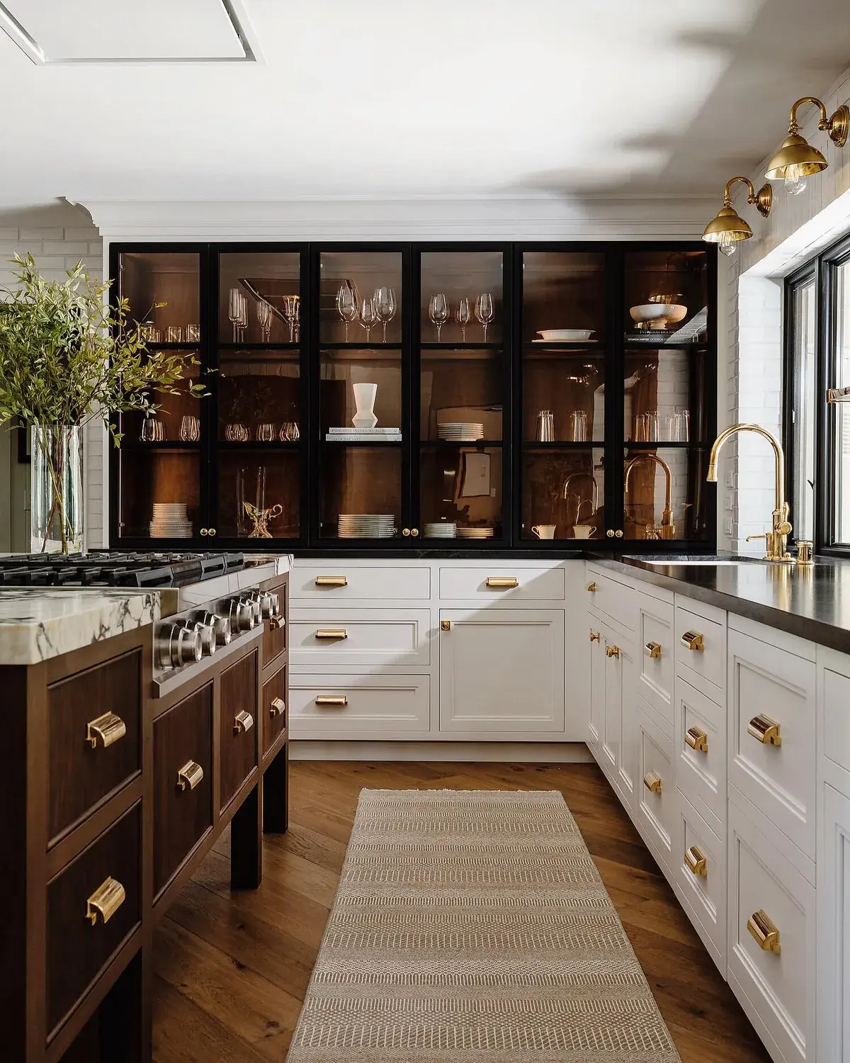 White kitchen with black framed glass wall cabinets, brass lights and brass tap