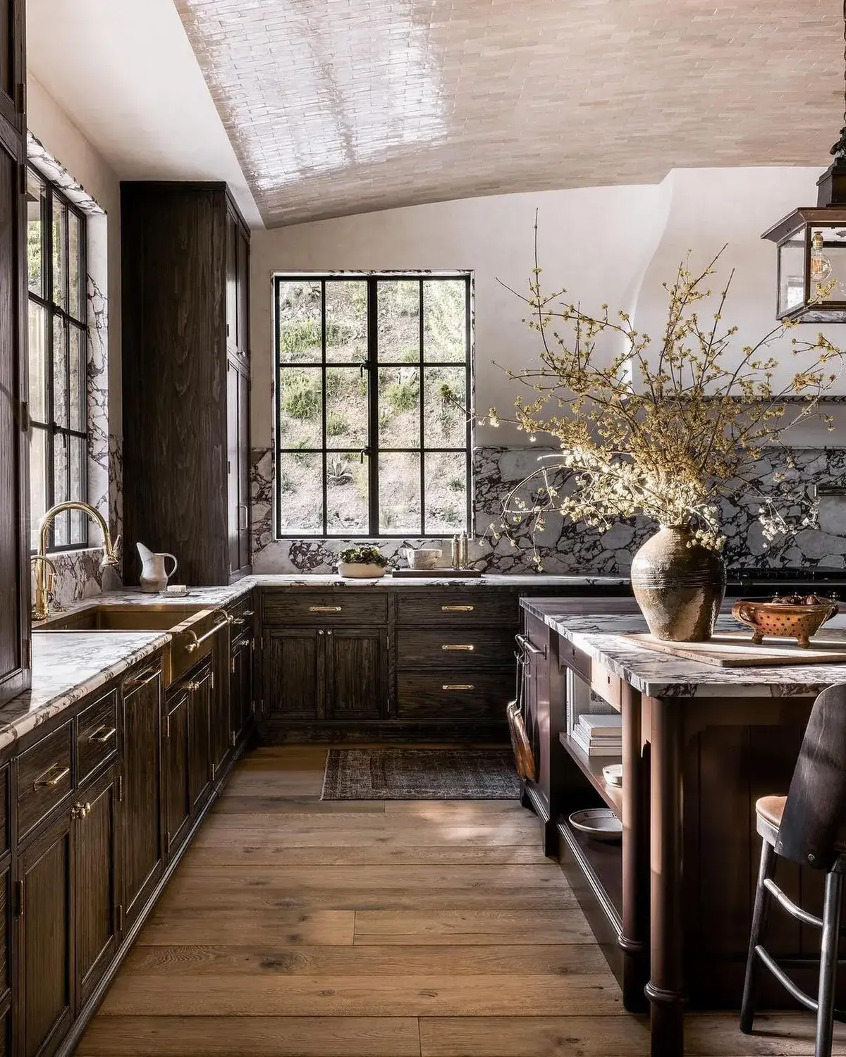 Dark stained kitchen with veined marble tops, brass tap and black steel windows