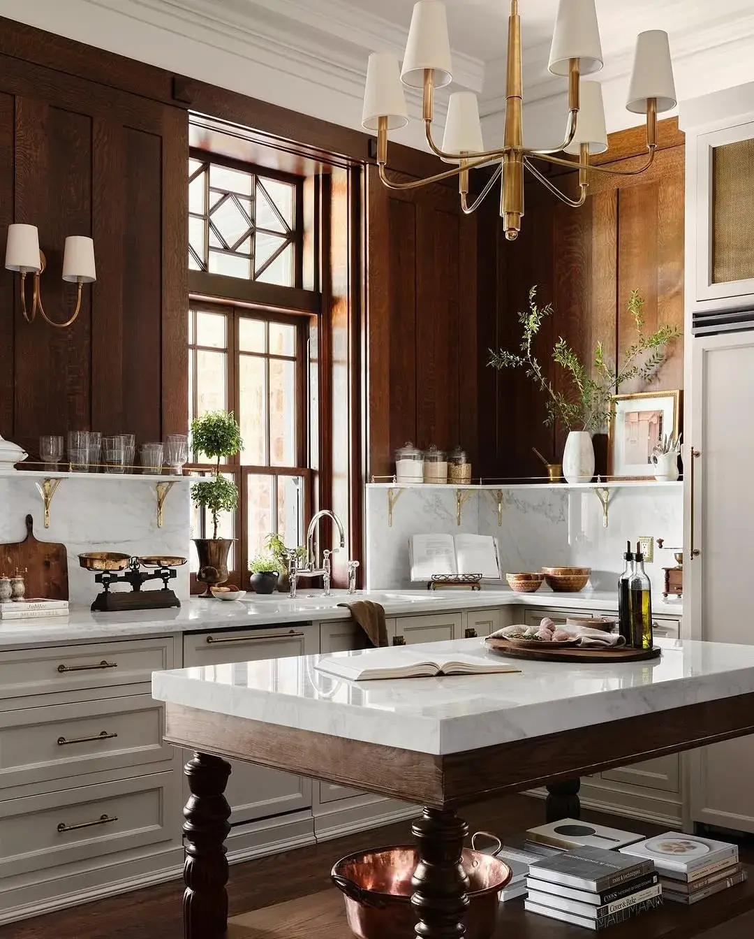 Dark panelled kitchen with a marble island, marble shelf and brass chandelier