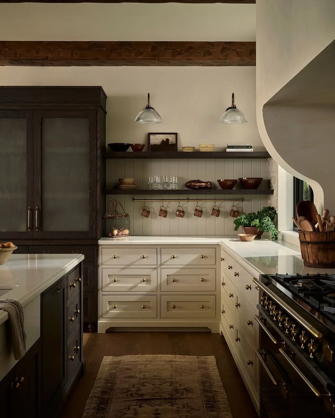 Cream kitchen with dark timber shelves, brass rail and glass pendants