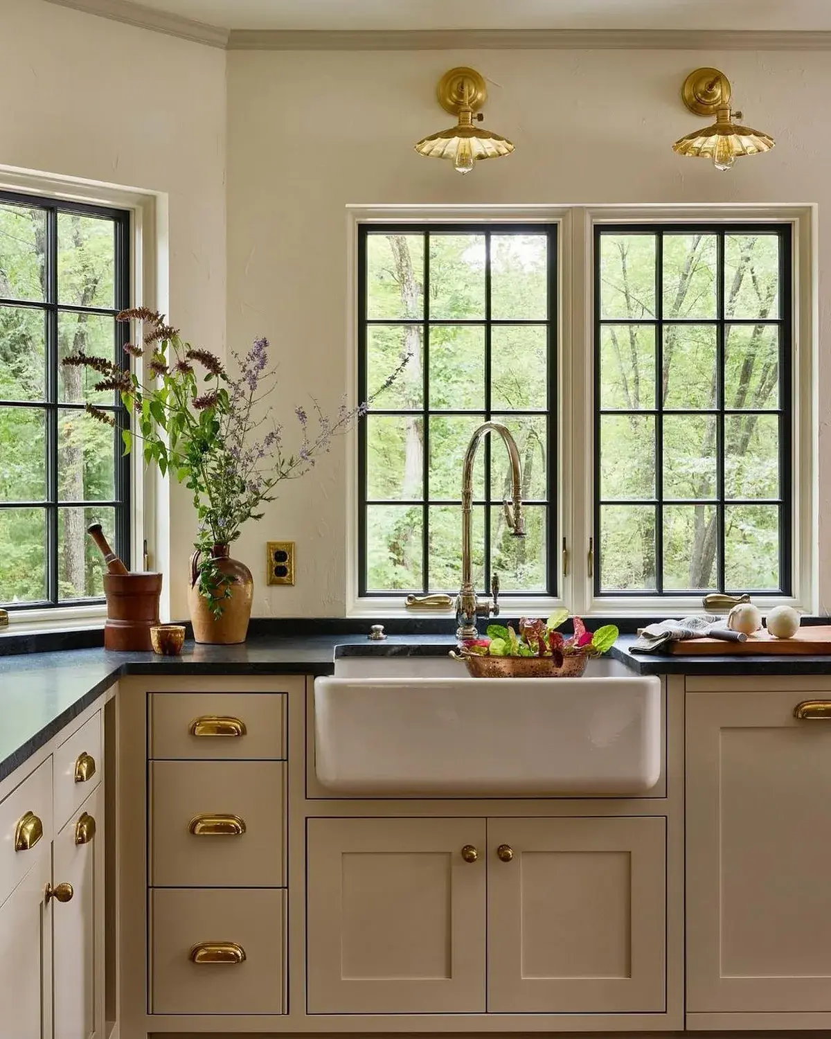 Cream kitchen with a white farmhouse sink, black windows and brass wall lights
